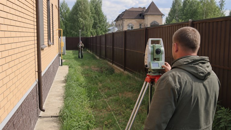 Геодезист измеряет спорное здание рядом с границей участка